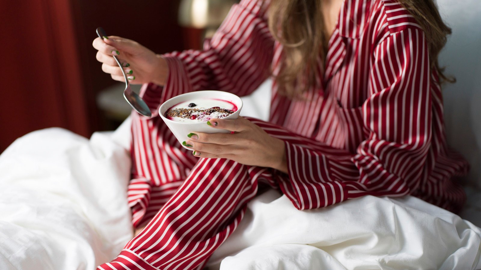 Flicka i röd och vit randig pyjamas äter frukost i hotellsäng
