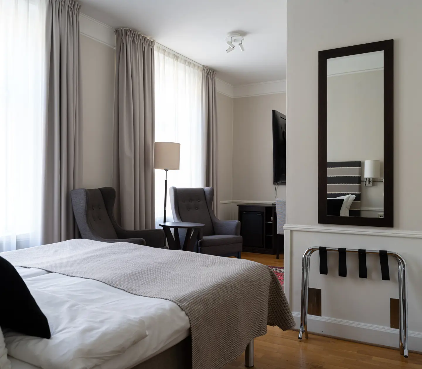 Hotellrum med dubbelsäng, spegel, skrivbord och tv
