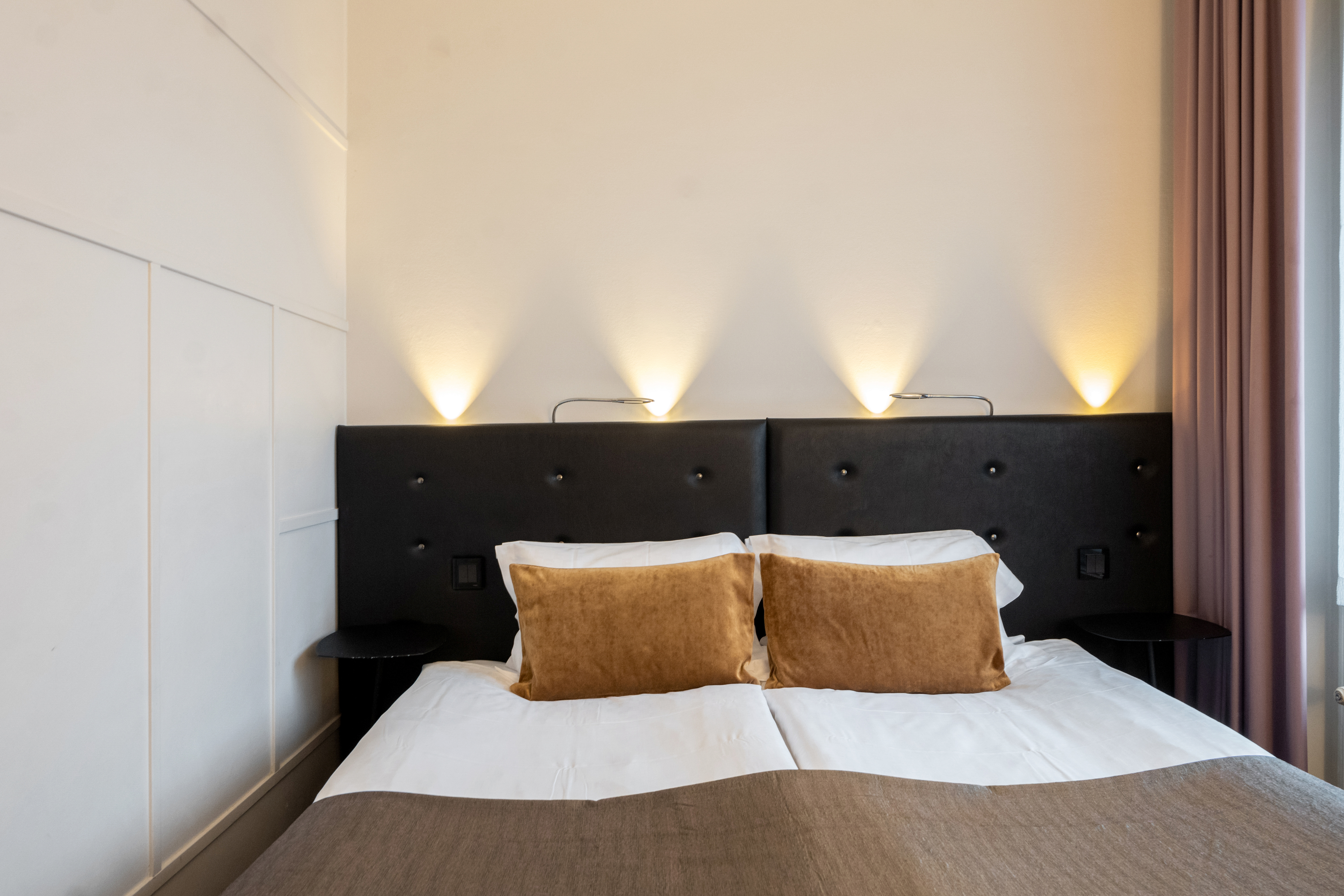 Hotellrum med fönster, dubbelsäng med svart sänggavel, lampor och gula kuddar