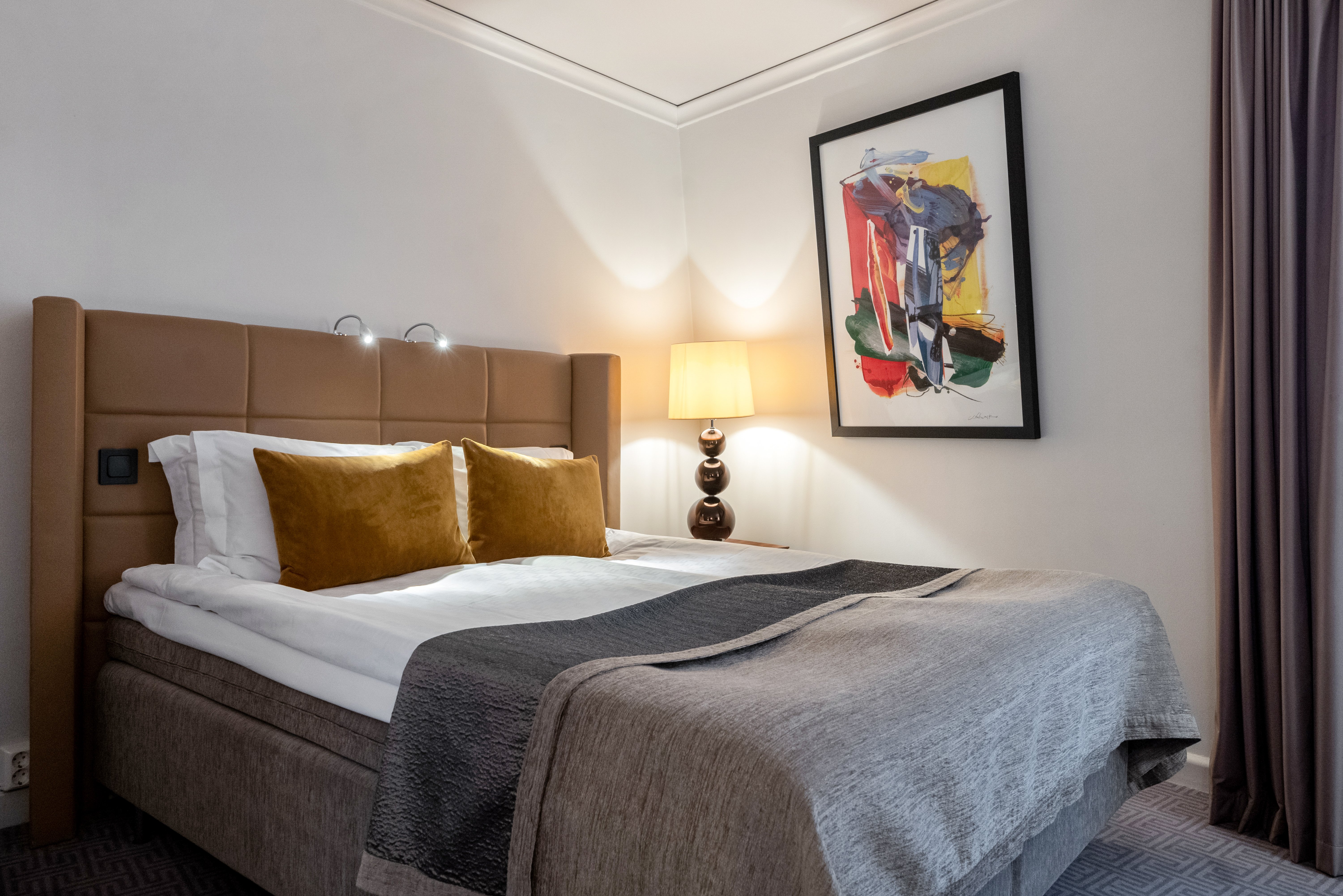 Mysigt hotellrum med dubbelsäng med gul sänggavel, lampor och tavla