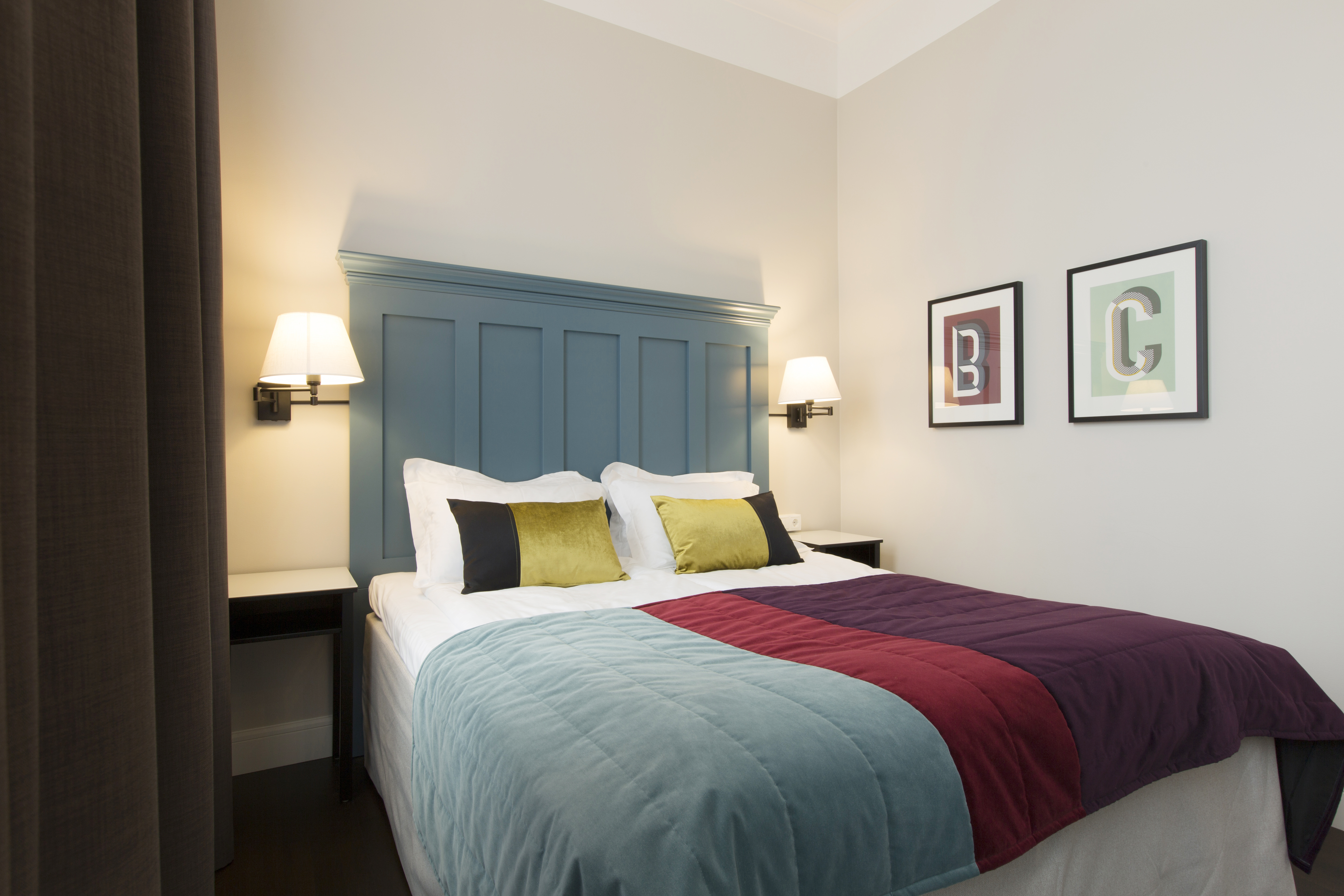 Ljust hotellrum med säng, stor blå sänggavel och sänglampor