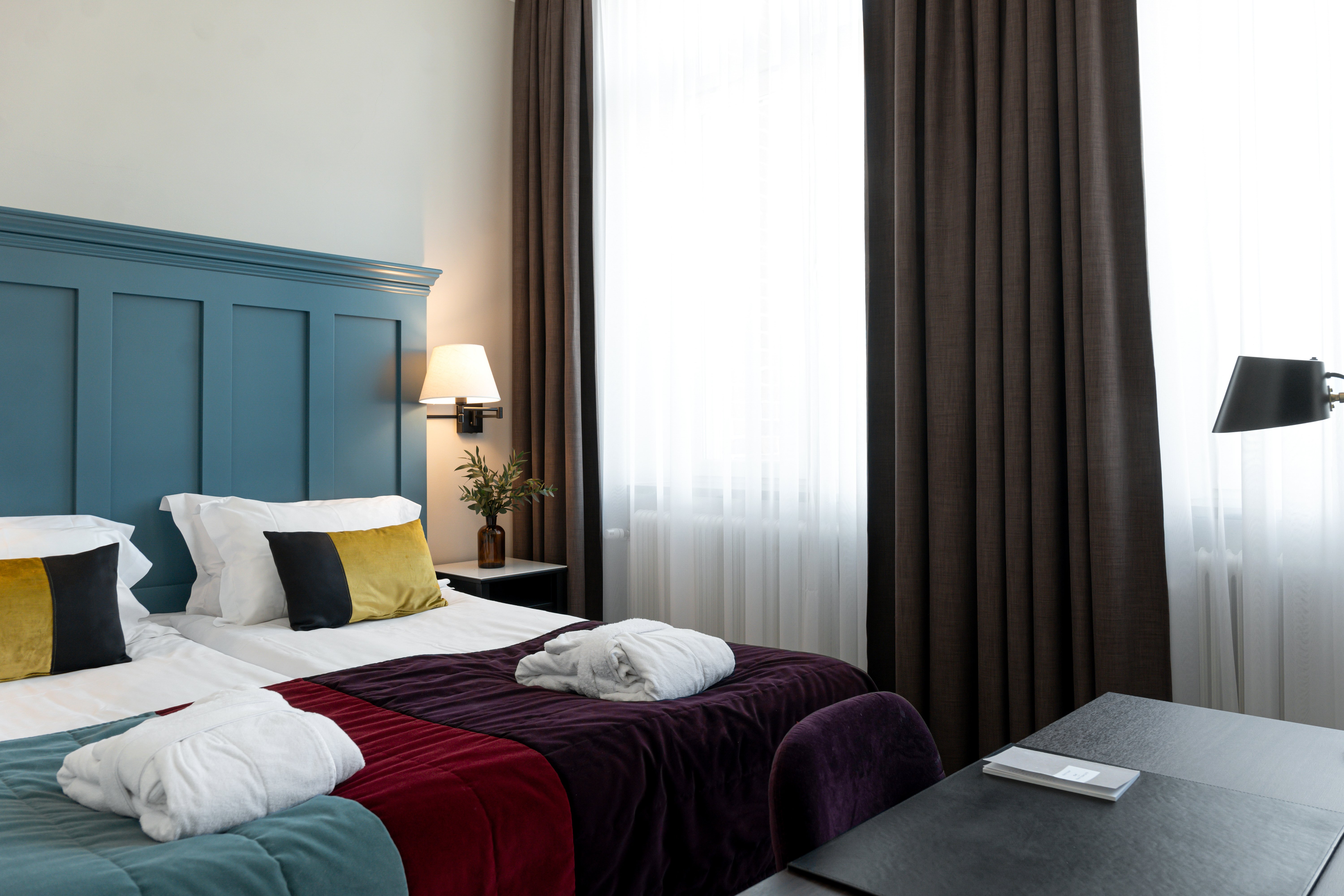 Ljust hotellrum med säng, stor blå sänggavel och morgonrockar