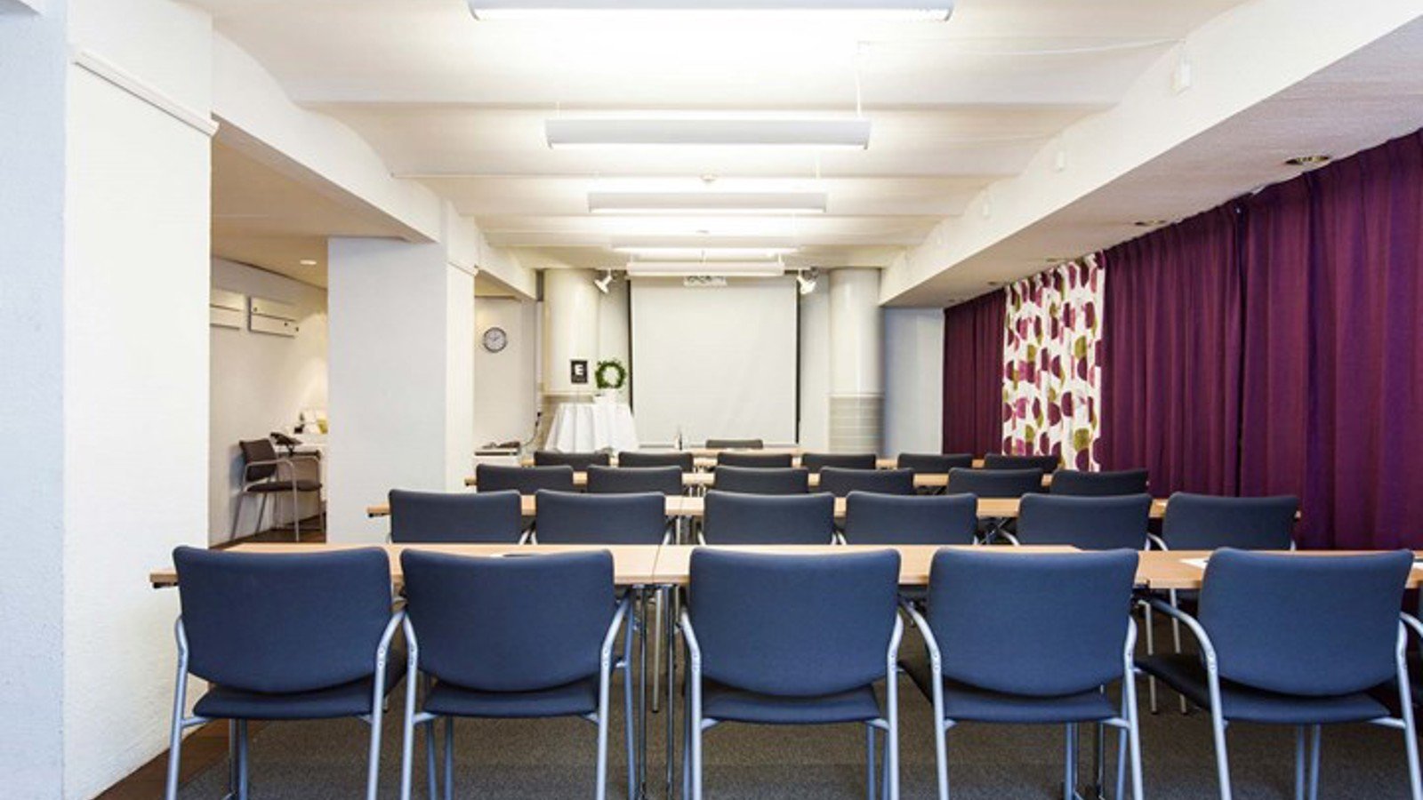 Konferensrum med skolsittning, blå stolar och lila draperi
