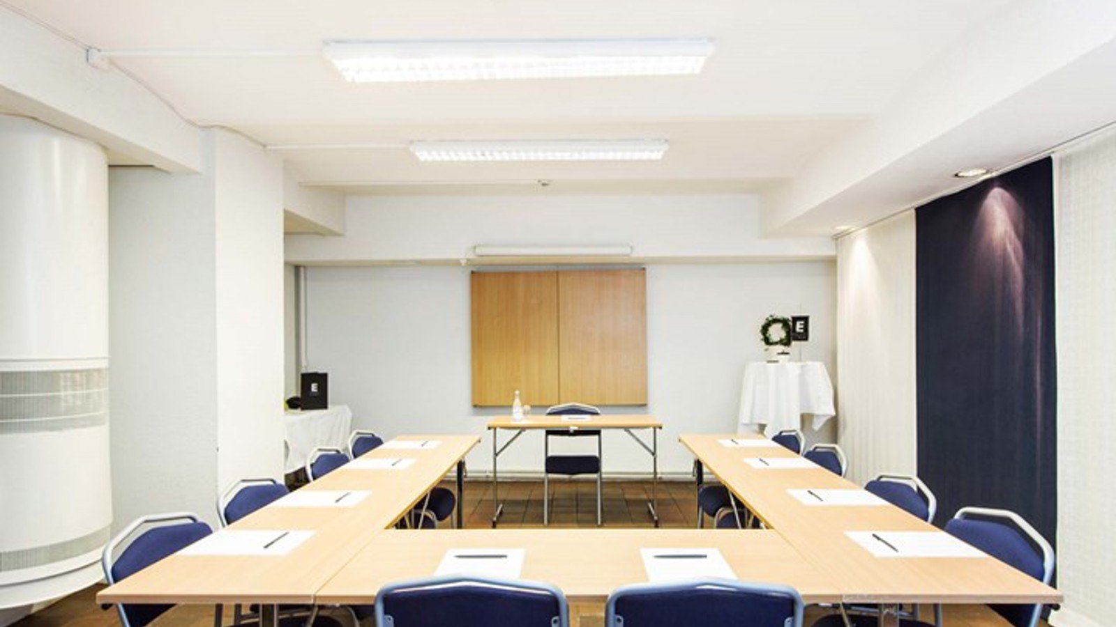 Konferensrum med u-sittning, vita väggar och ljusa träbord