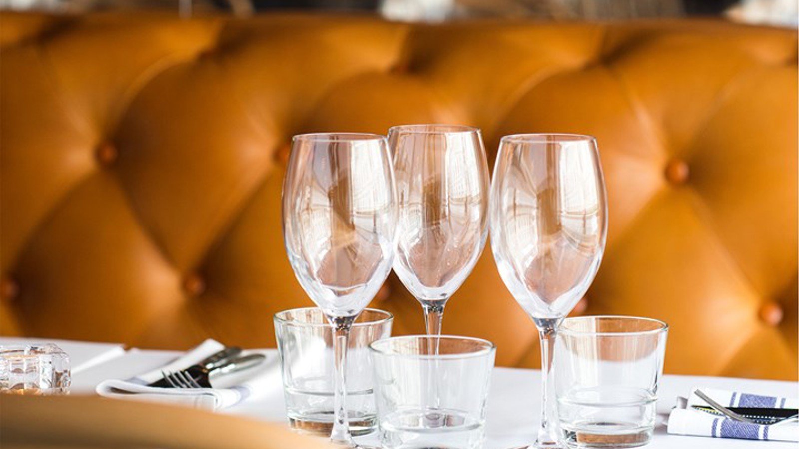 Three wine glasses on a table in front of a brown leather sofa