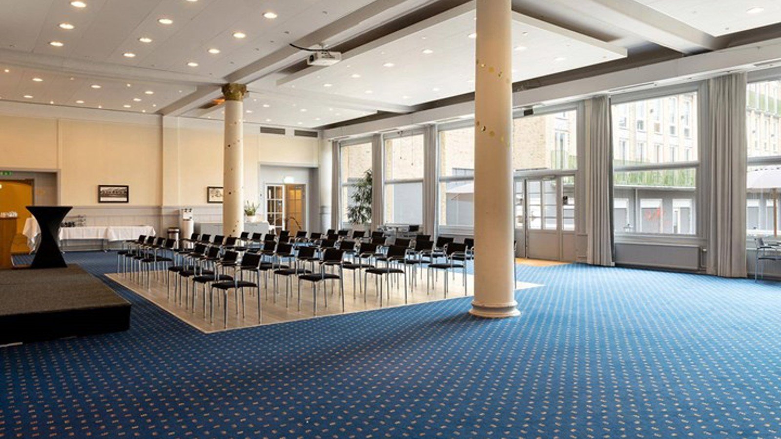 Large room with blue carpet, lined up chairs and large windows