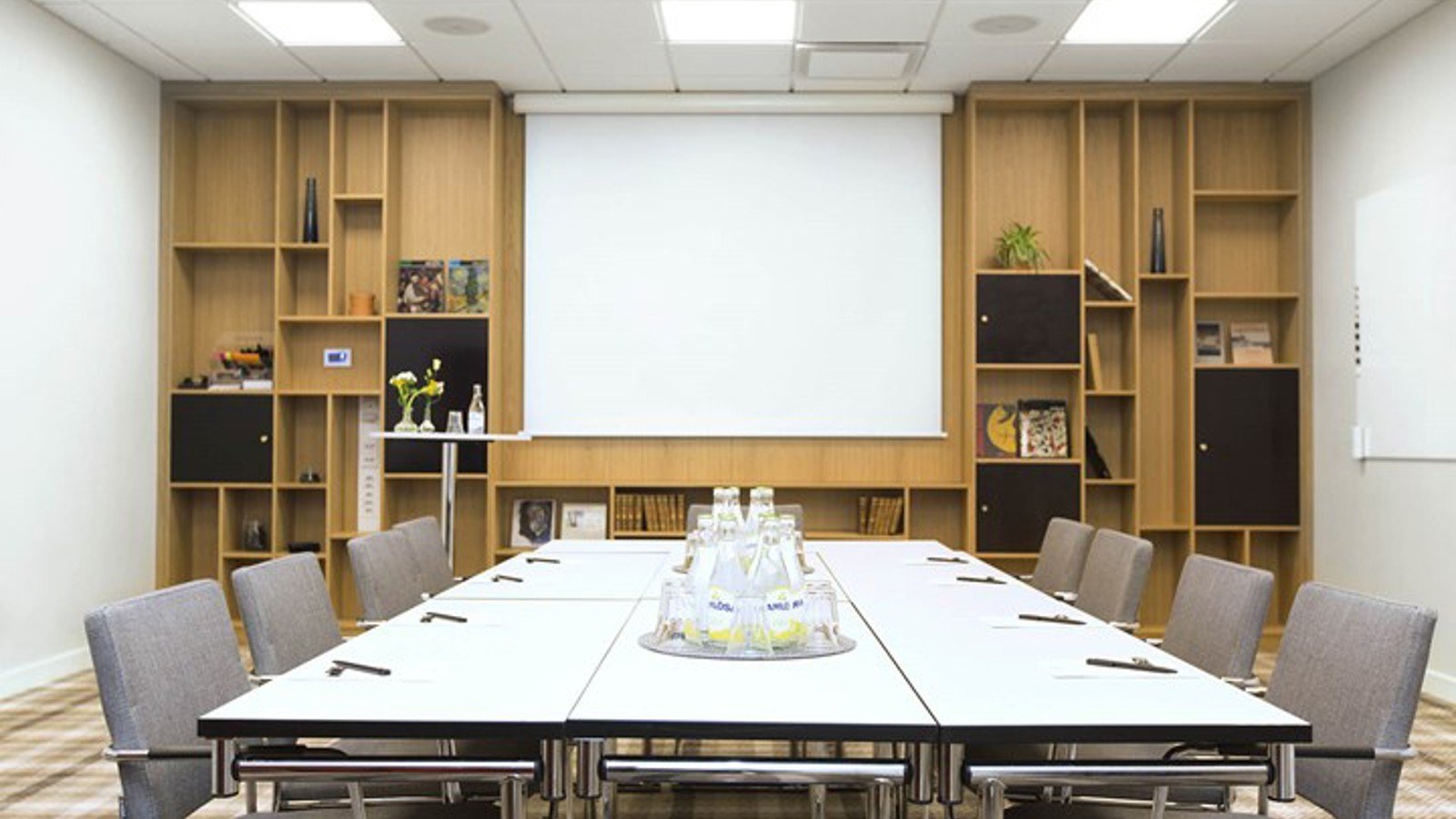 Konferensrum med styrelsesittning, grå stolar och bokhylla i trä