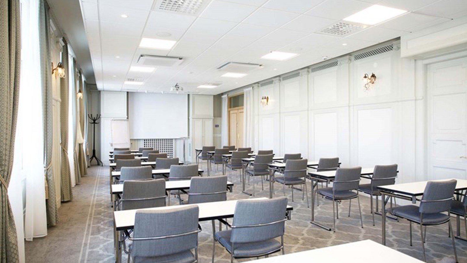Konferensrum med skolsittning, grå stolar, vita väggar och stora fönster