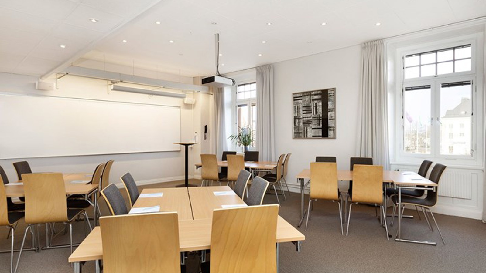 Konferensrum med ö-ar, vita väggar, träbord och grått golv