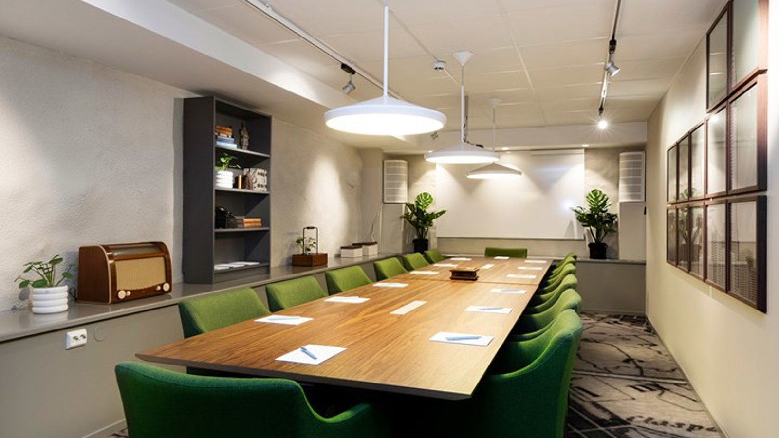 Konferensrum med styrelsesittning, mörkbrunt bord och gröna stolar