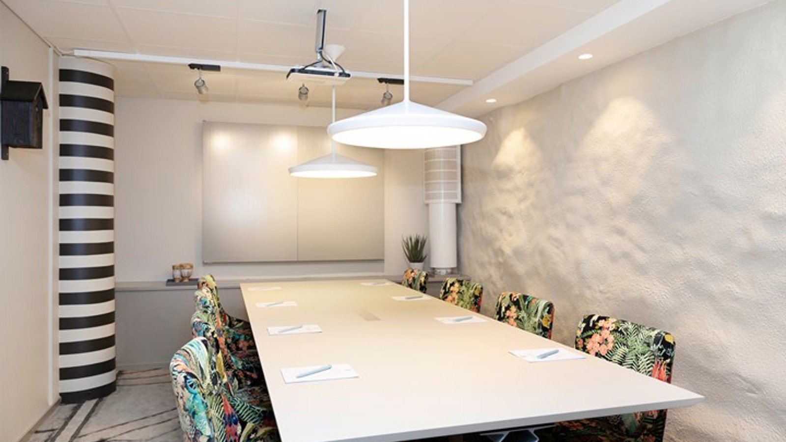 Konferensrum med styrelsesittning, vitt bord, vita väggar och mönstrade stolar