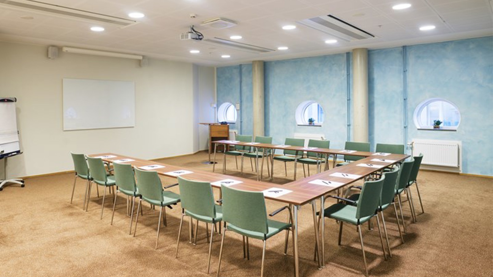 Konferensrum med u-sittning, ljusblå fondvägg och runda fönstrer