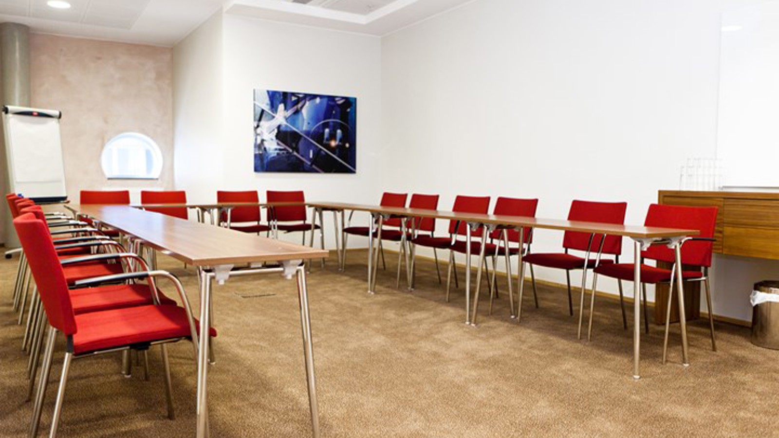 Konferensrum med u-sittning, röda stolar, ljusbrunt golv och vita väggar