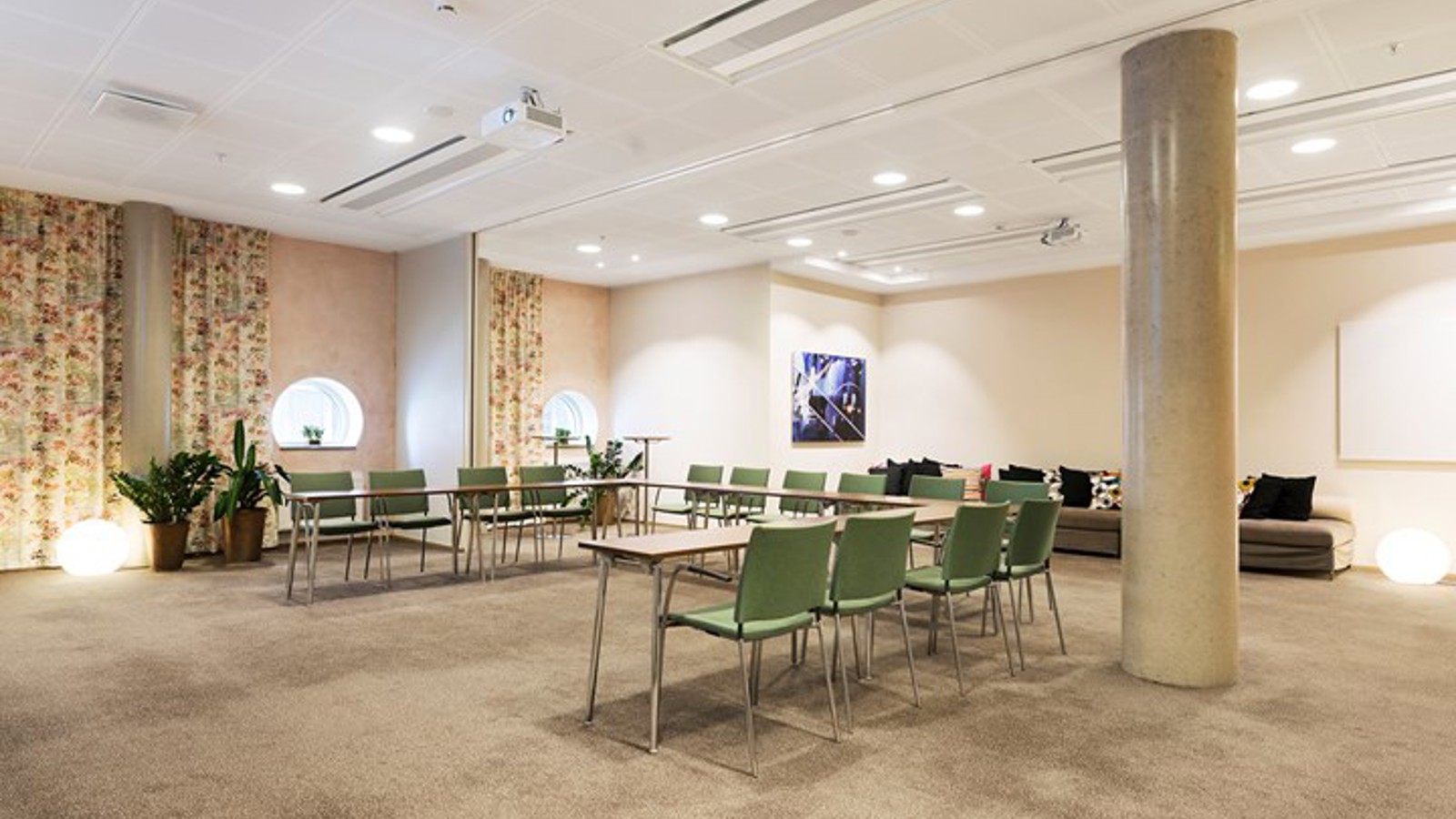 Konferensrum med u-sittning, ljusbrunt golv, gröna stolar och mönstrade draperier