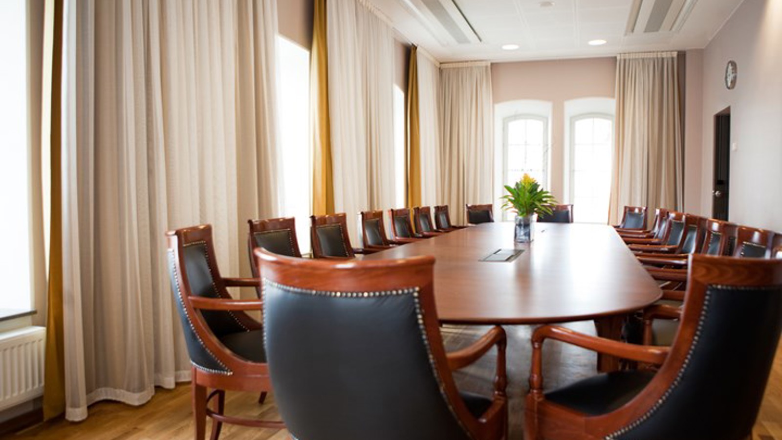 Konferensrum med styrelsesittning, brunt bord, bruna stolar med svart klädsel och stora fönster