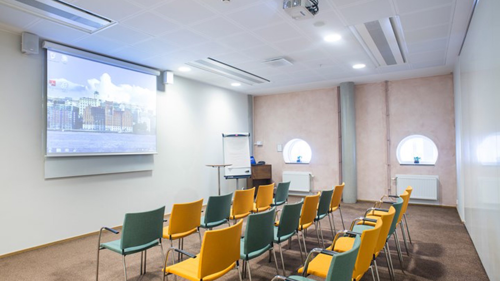 Konferensrum med biosittning, gula och blå stolar, vita väggar och projektor