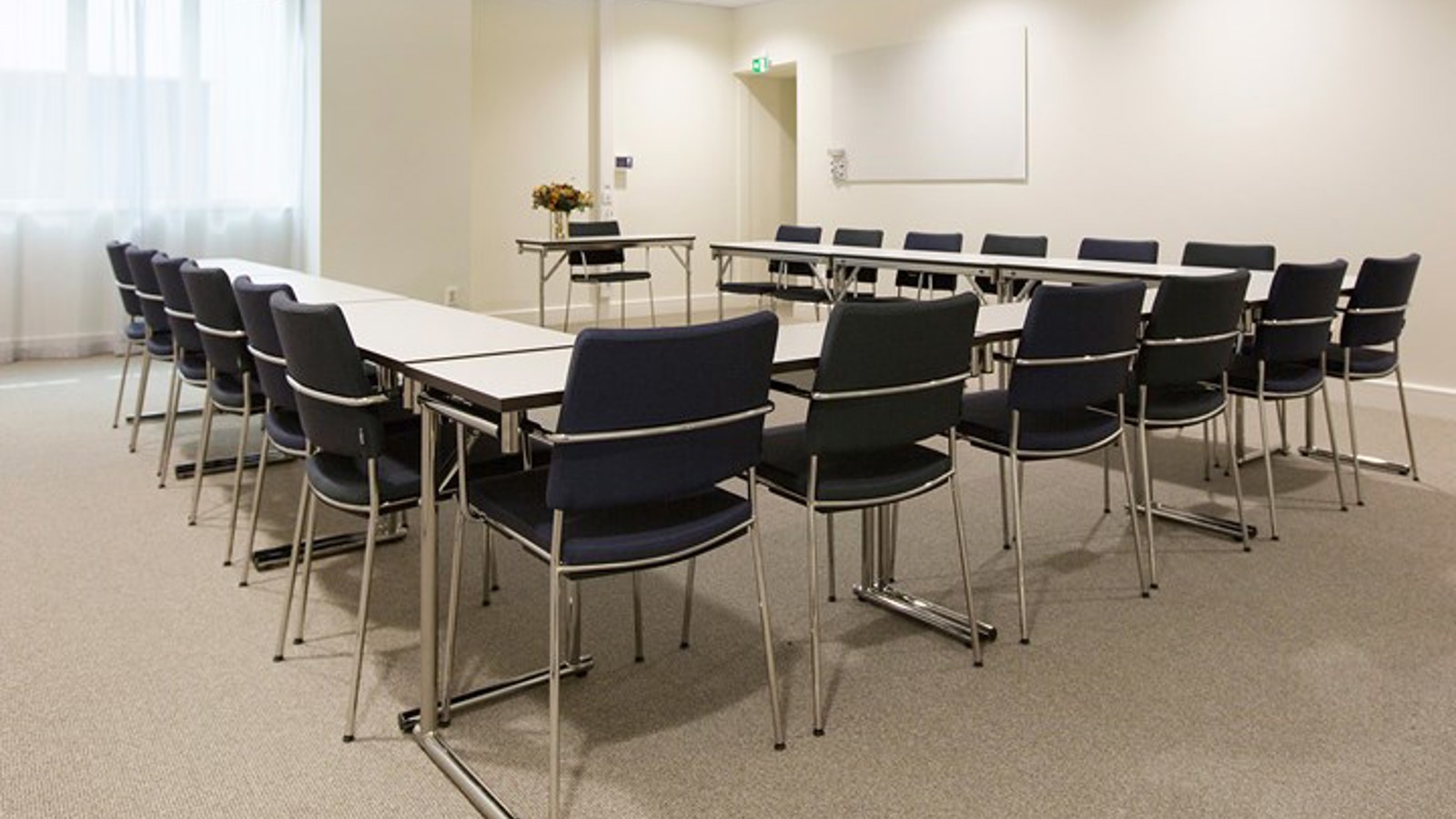 Ljust konferensrum med u-sittning, vita väggar och svarta stolar