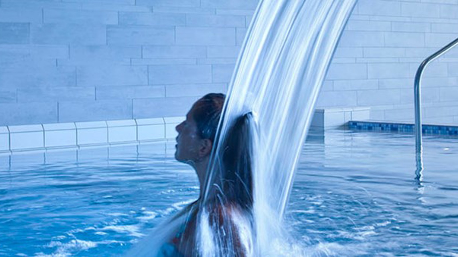 Kvinna står under en vattenfallsfontän i en pool