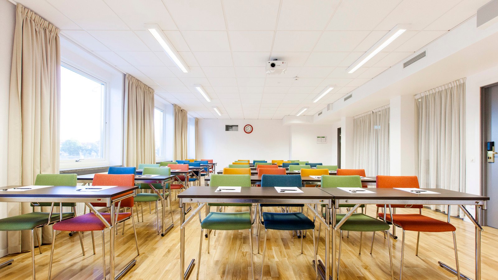 Big room with wooden floor boards and many colourful chairs