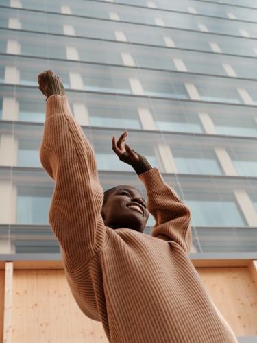 Kvinna som sträcker upp armarna i luften framför hotellfasad