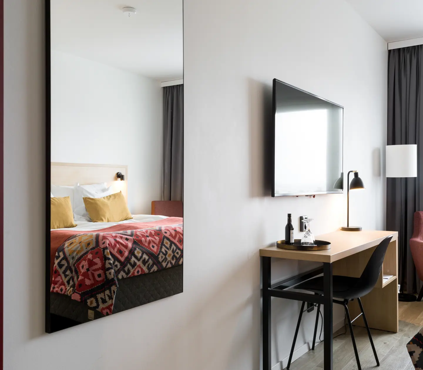 Bright hotel room with mirror, double bed and TV