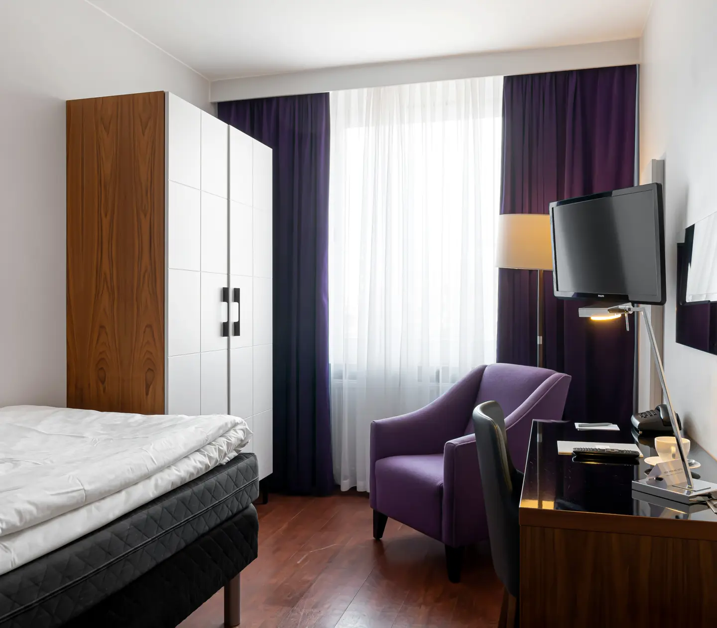 Hotel room with single bed, desk and wardrobe