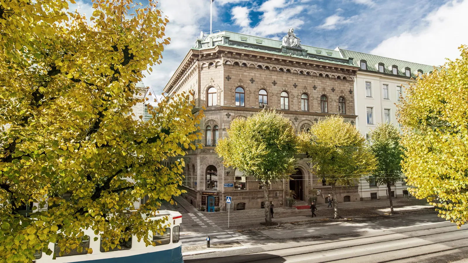 Fina fasaden av Elite Plaza Hotel i Göteborg med träd och spårvagn framför
