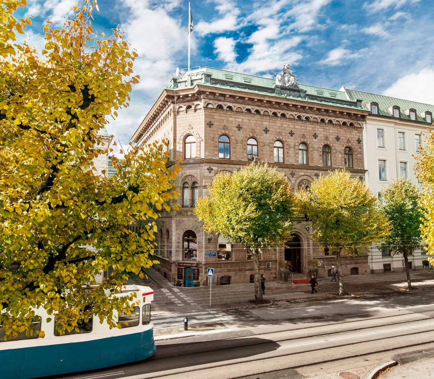 Fina fasaden av Elite Plaza Hotel i Göteborg med träd och spårvagn framför