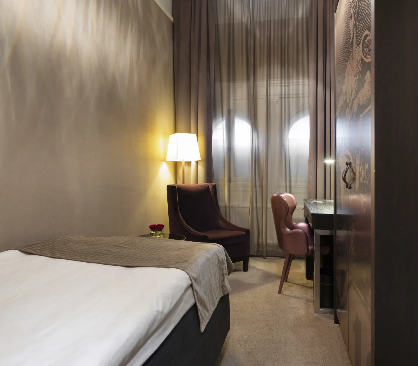 Small hotel room with bed, armchair and desk