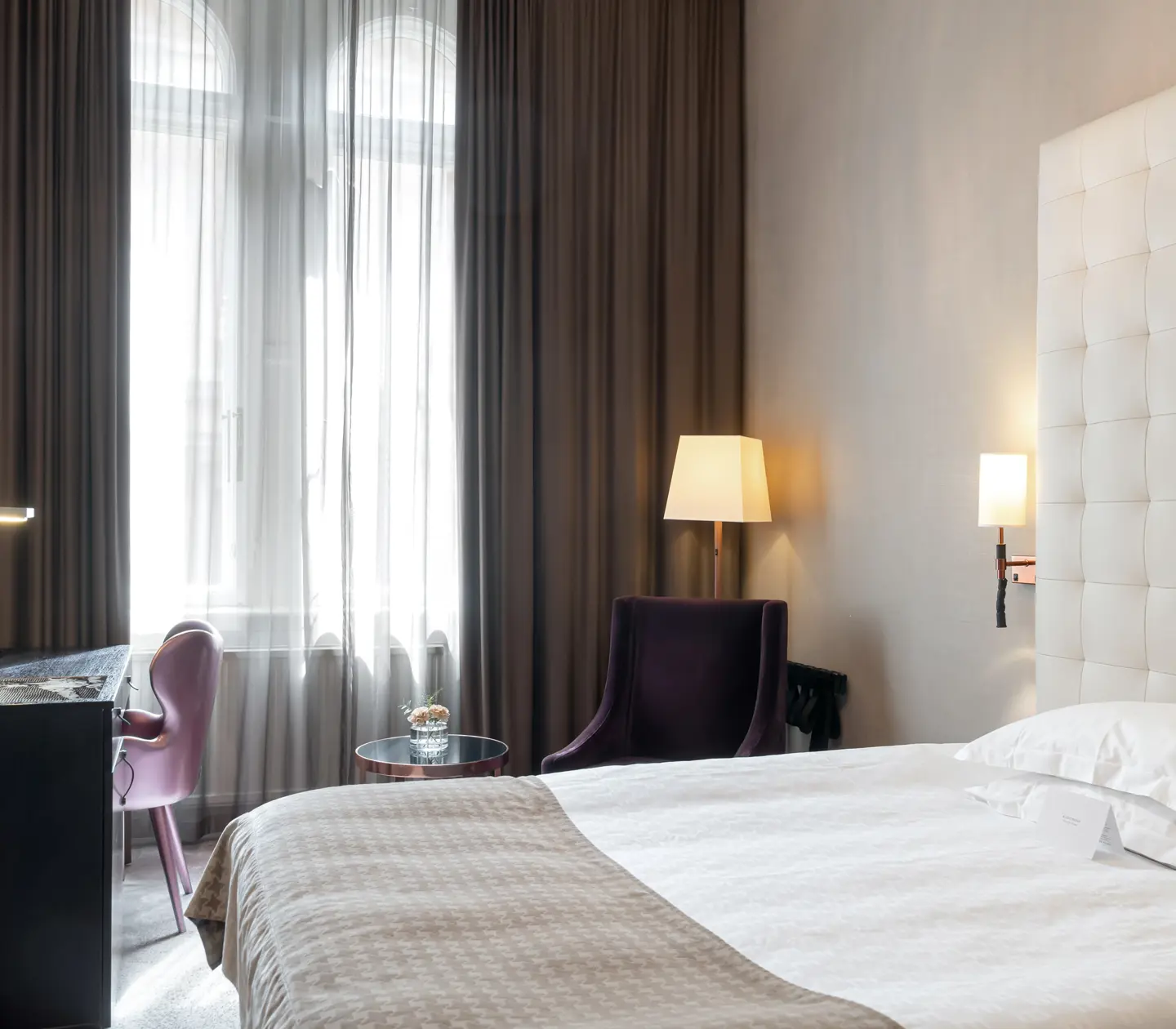 Bright hotel room with bed, large headboard and desk