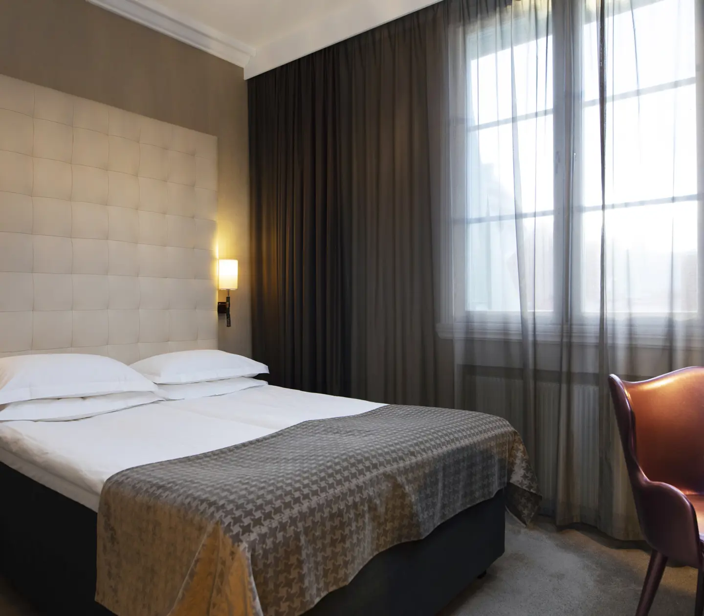 Hotel room with bed, large headboard and curtains along the wall