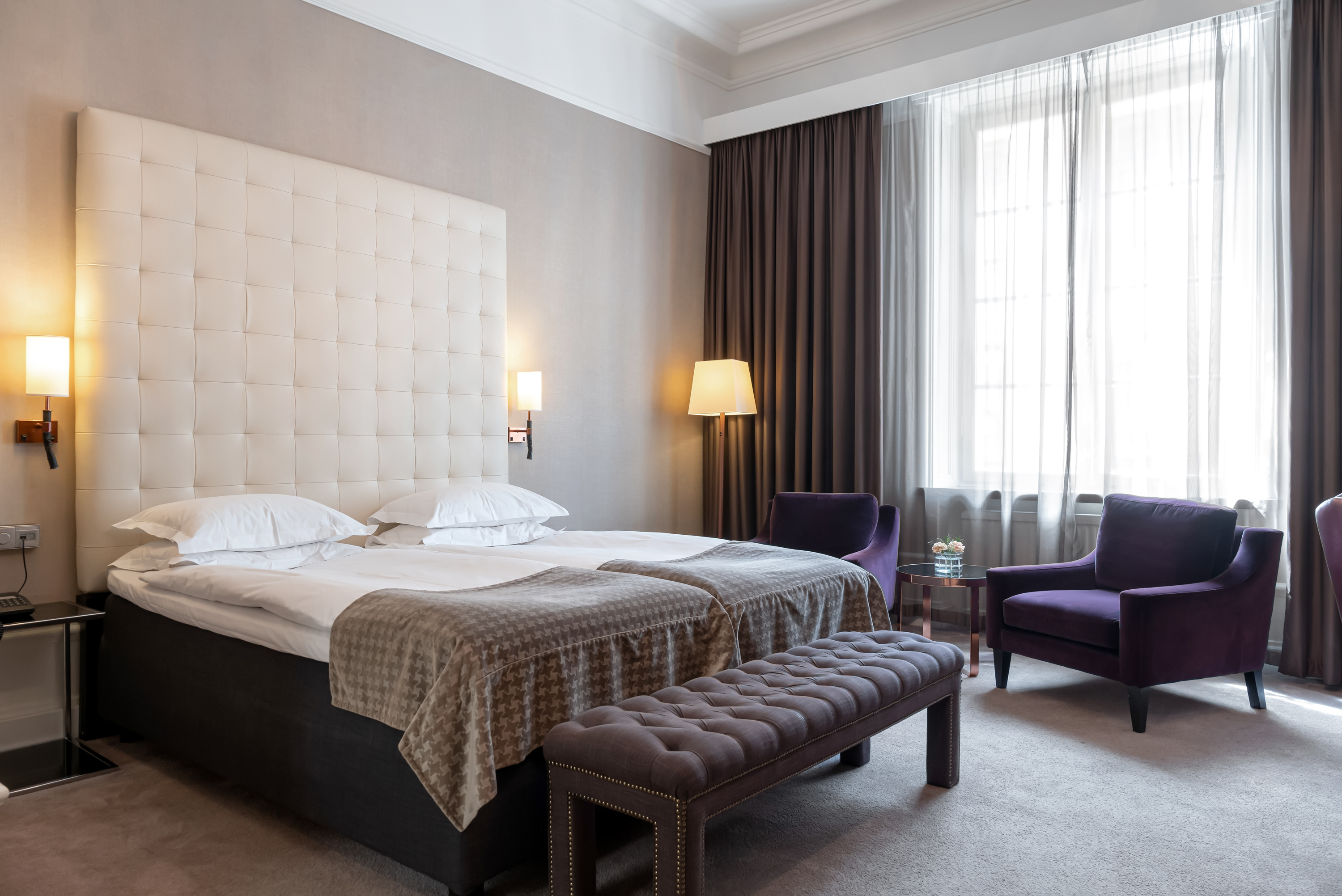 Hotel room with bed, large headboard and purple armchairs