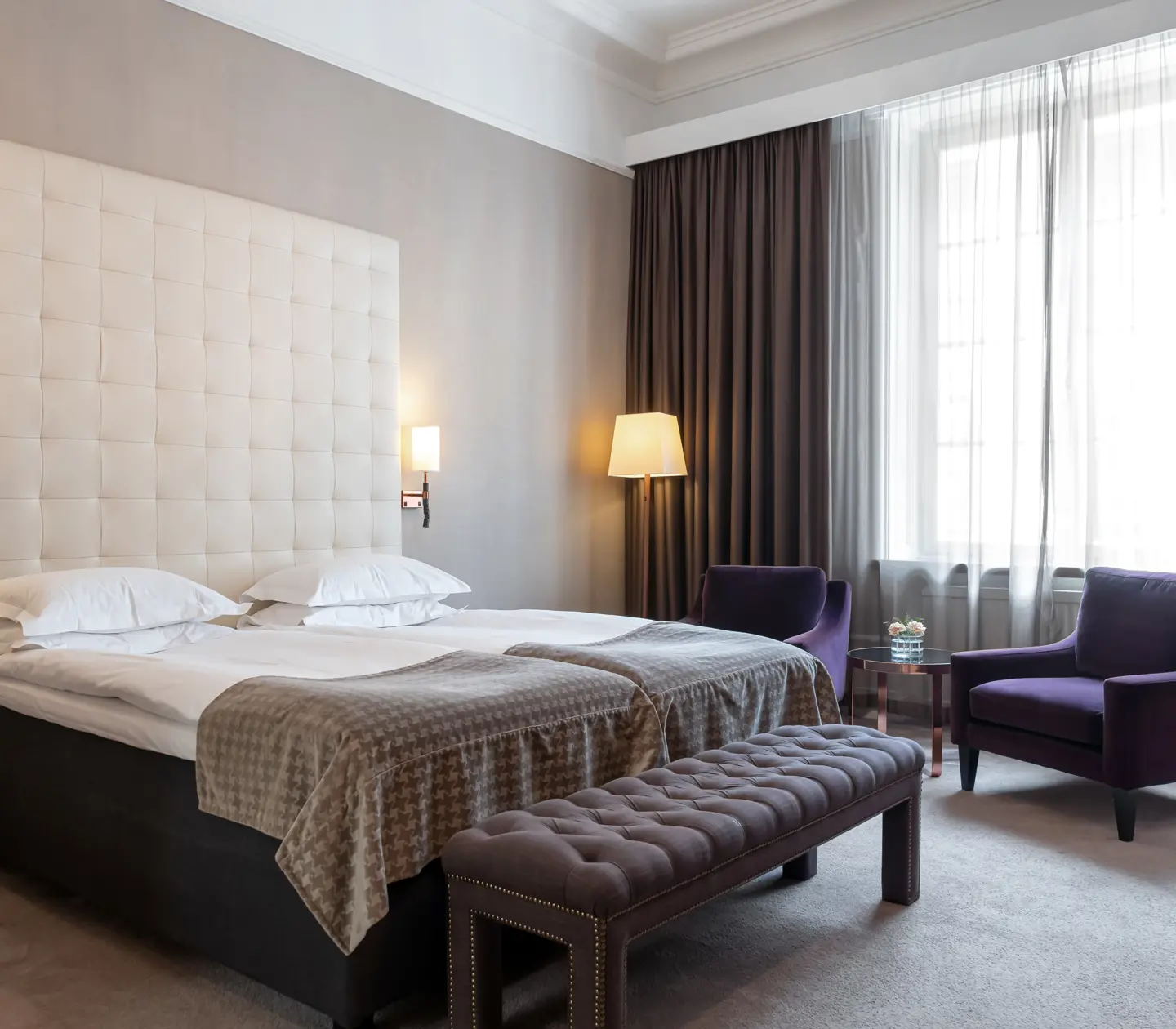 Hotel room with bed, large headboard and purple armchairs