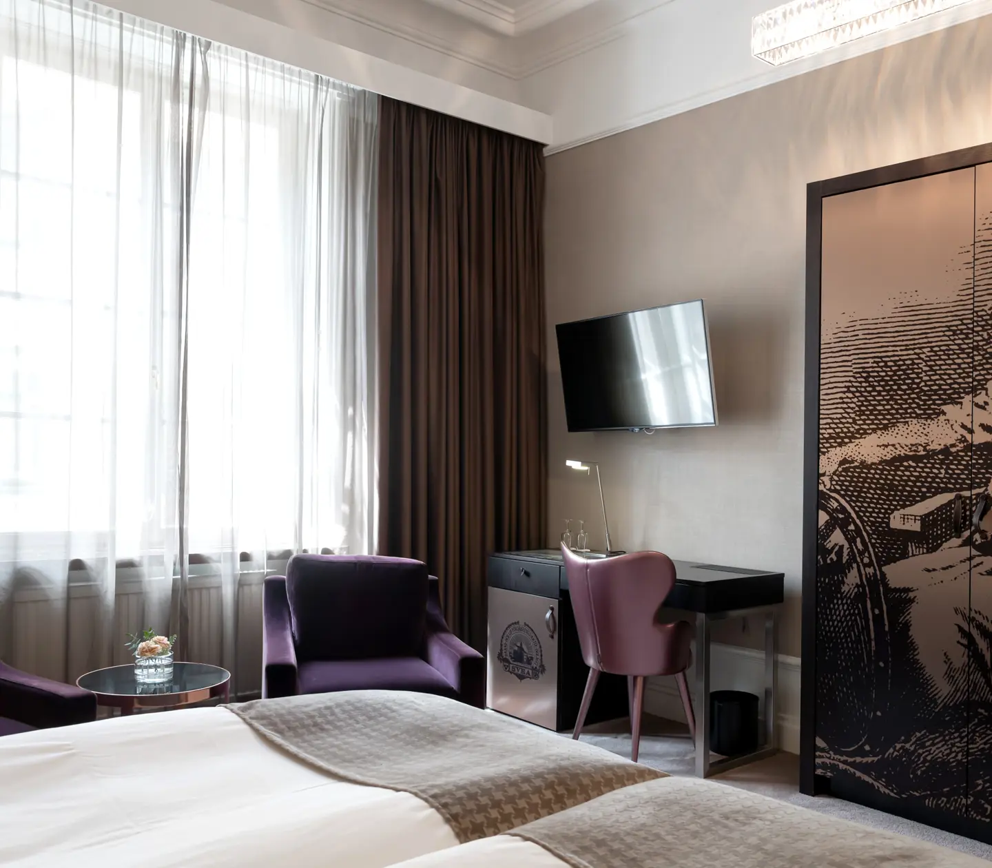 Bright hotel room with purple armchairs, desk and wardrobe