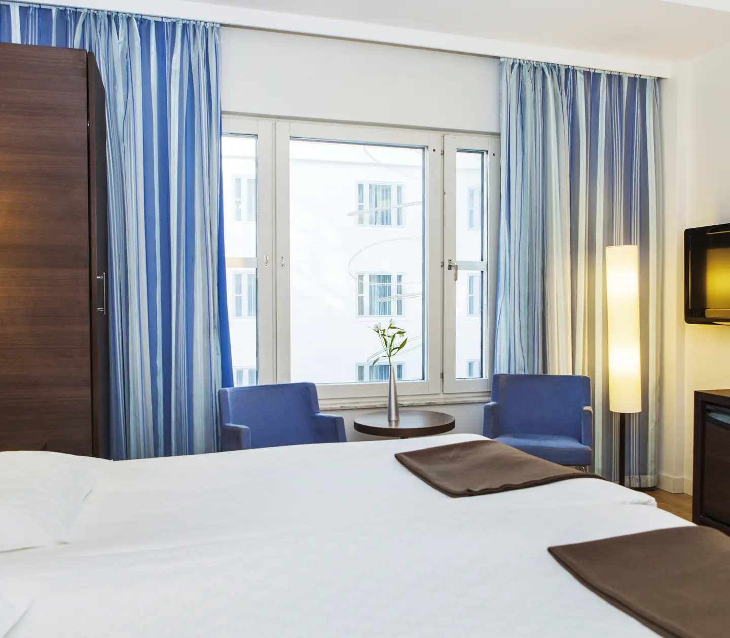 Bright hotel room with blue curtains, blue armchairs and bed