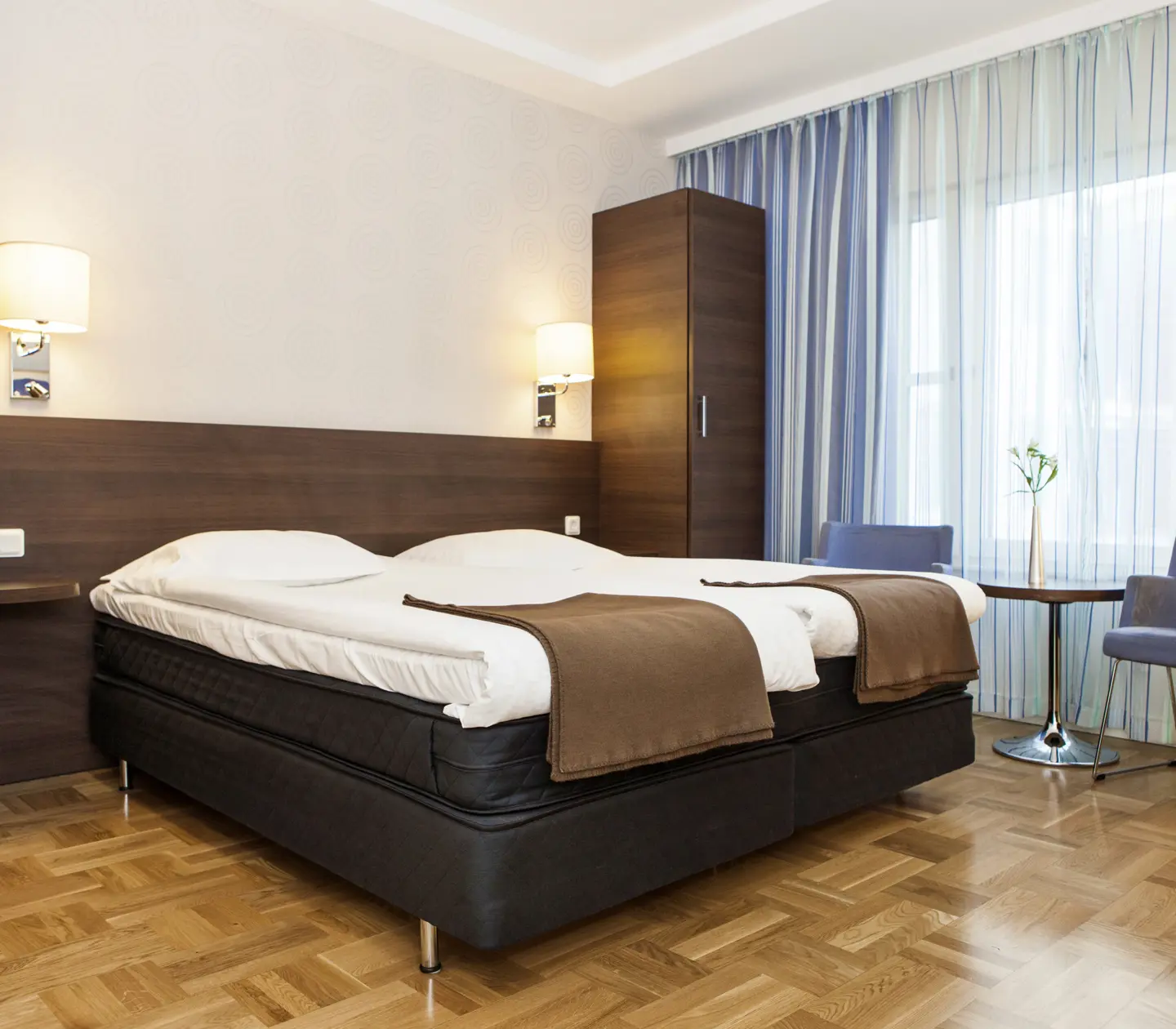 Bright hotel room with blue curtains, blue armchairs and bed