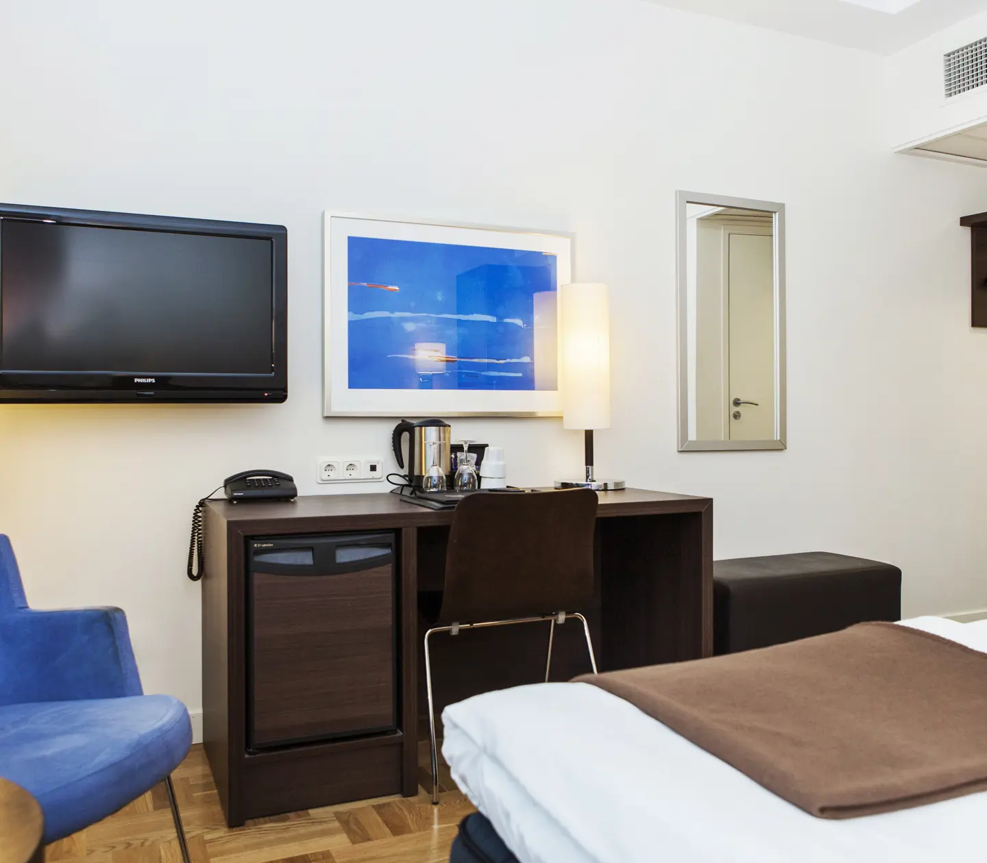 Bright hotel room with desk, TV and blue armchair