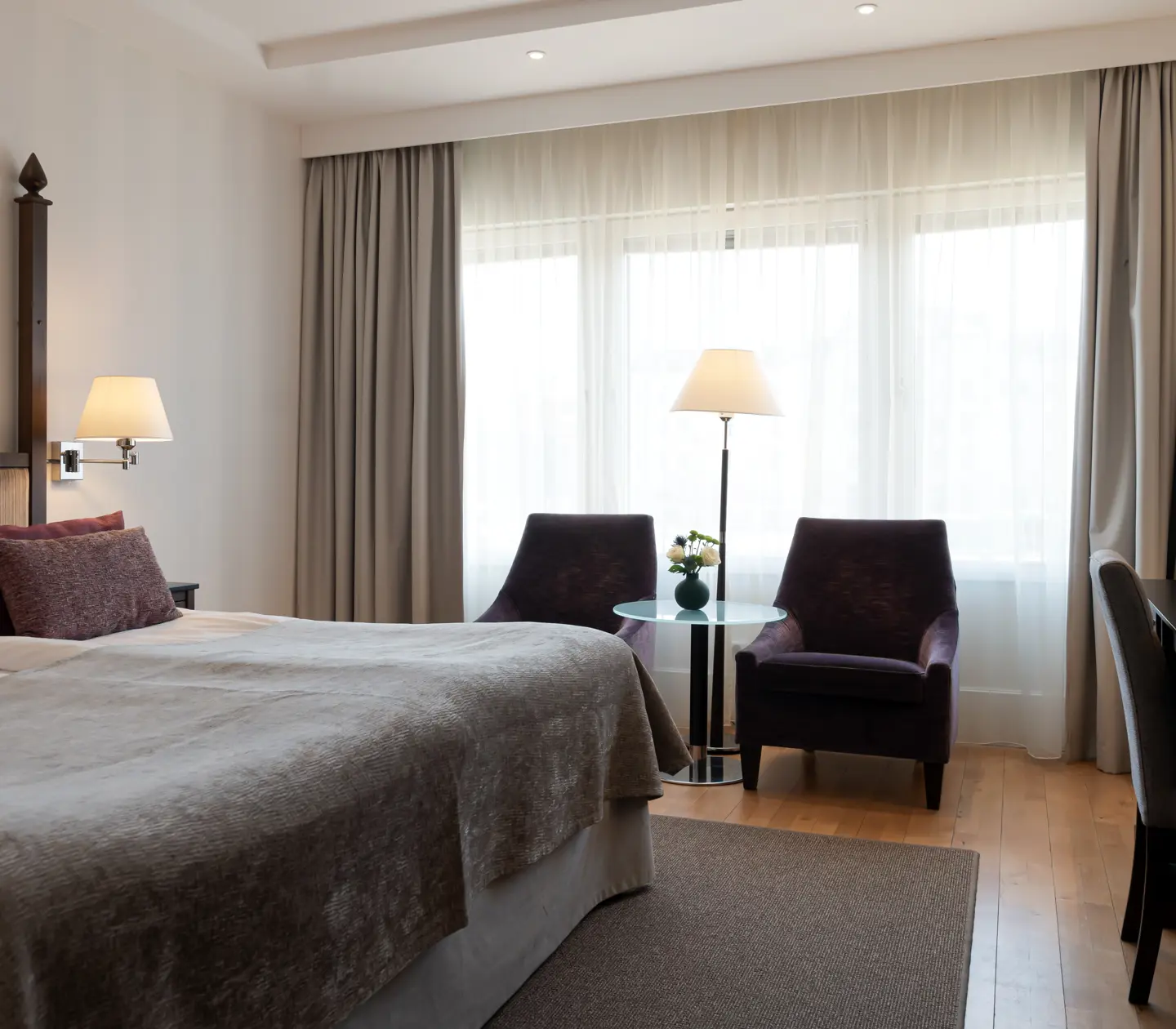 Bright hotel room with double bed, armchairs and window