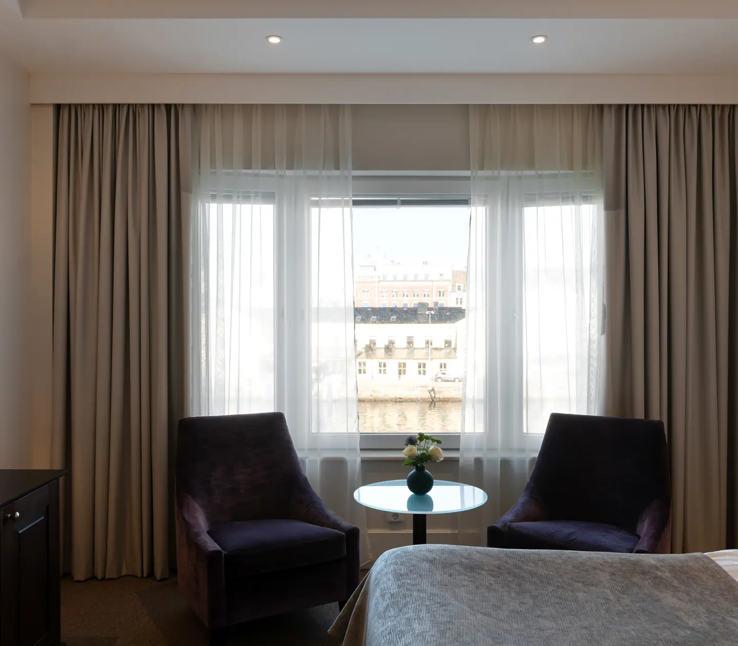 Bright hotel room with desk, armchairs and window overlooking the harbor