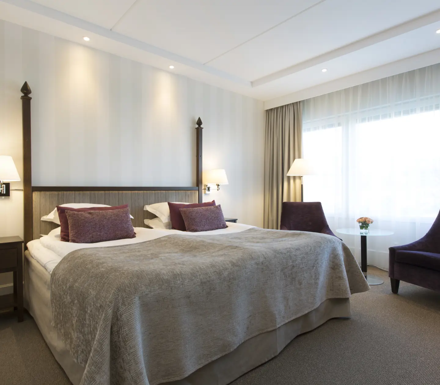 Bright hotel room with bed, armchairs and window