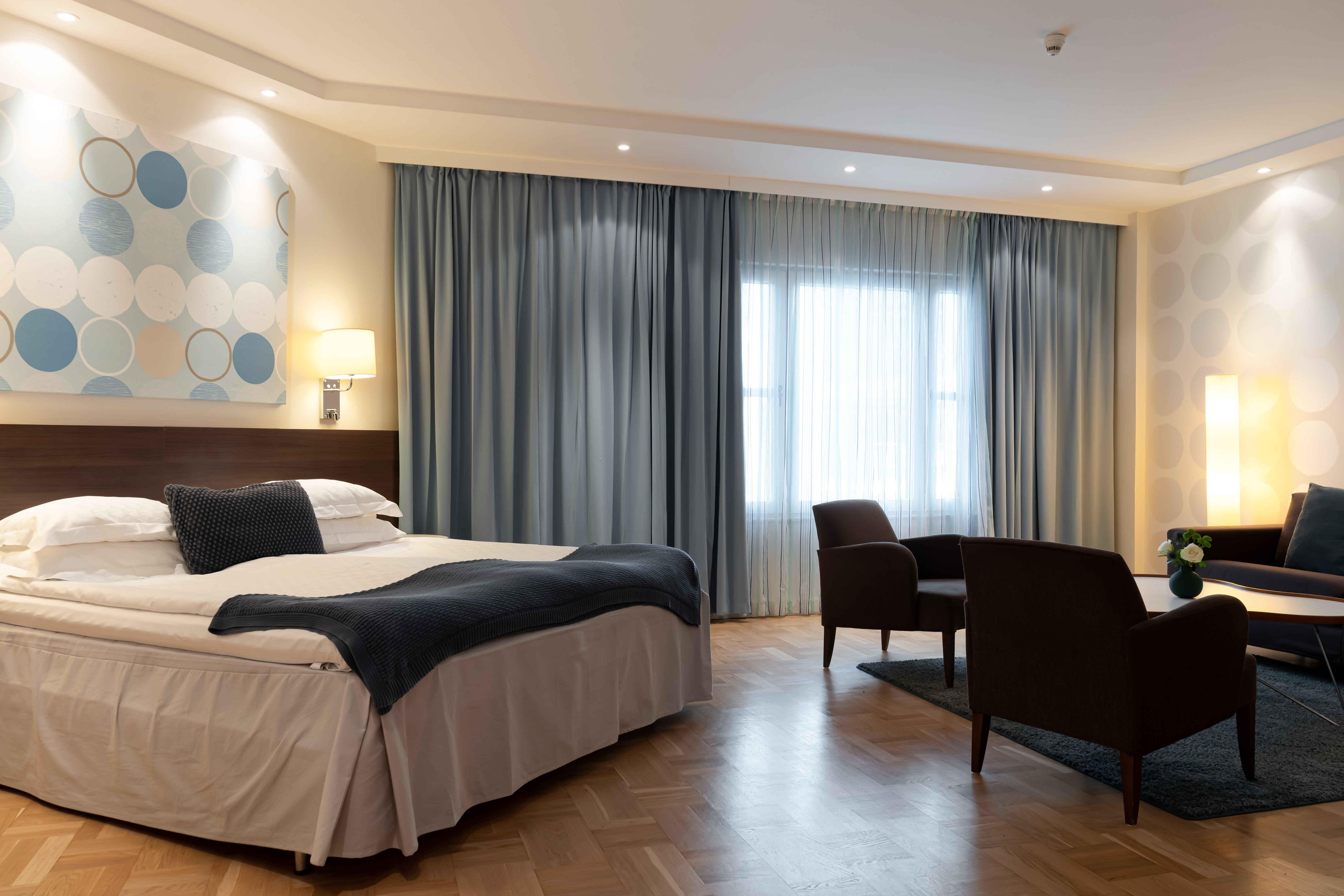 Ljust hotellrum med dubbelsäng, soffgrupp och blå gardiner