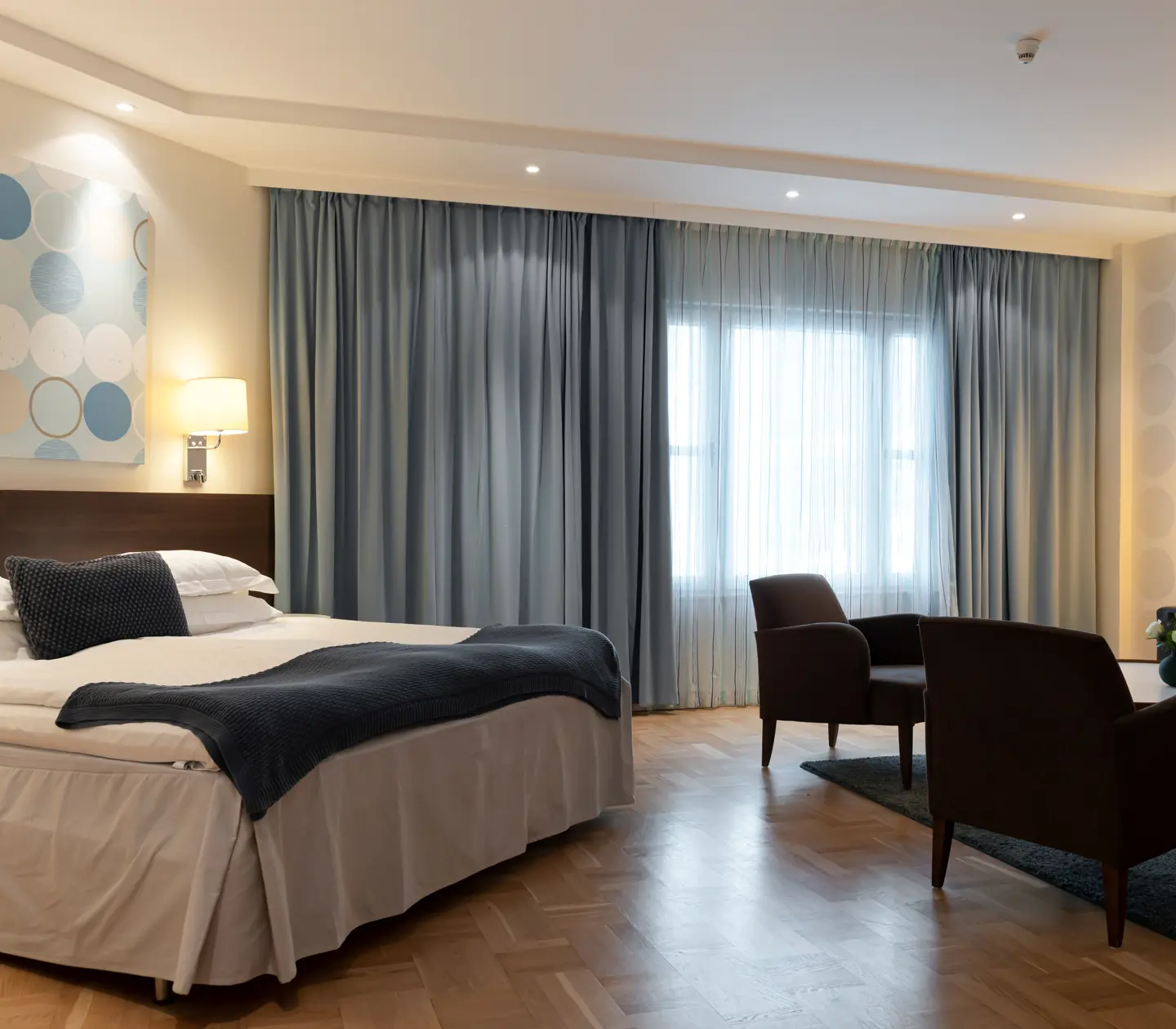 Bright hotel room with double bed, sofa group and blue curtains