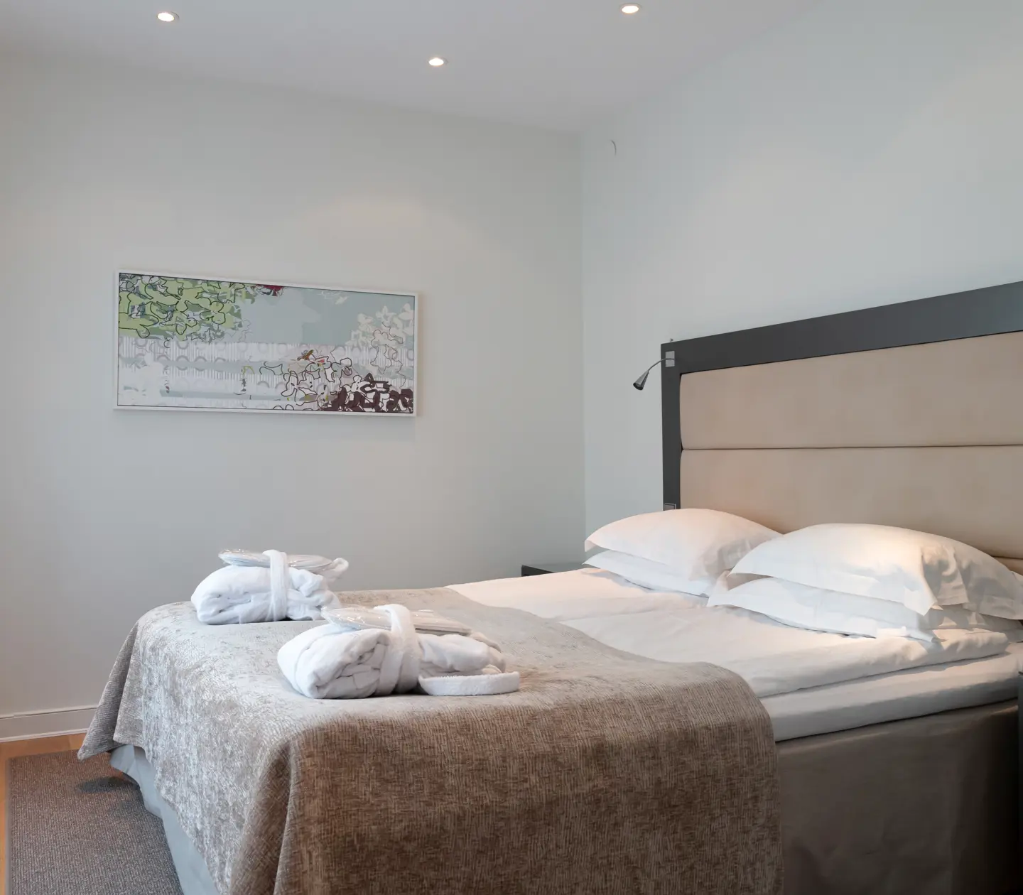 Bright hotel suite with bed, headboard and bathrobes