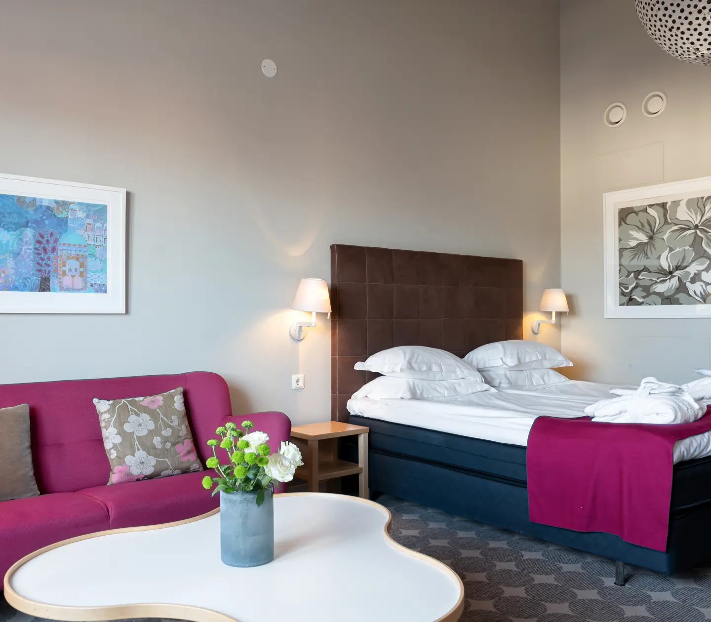 Bright hotel suite with sofa, bed and dark headboard