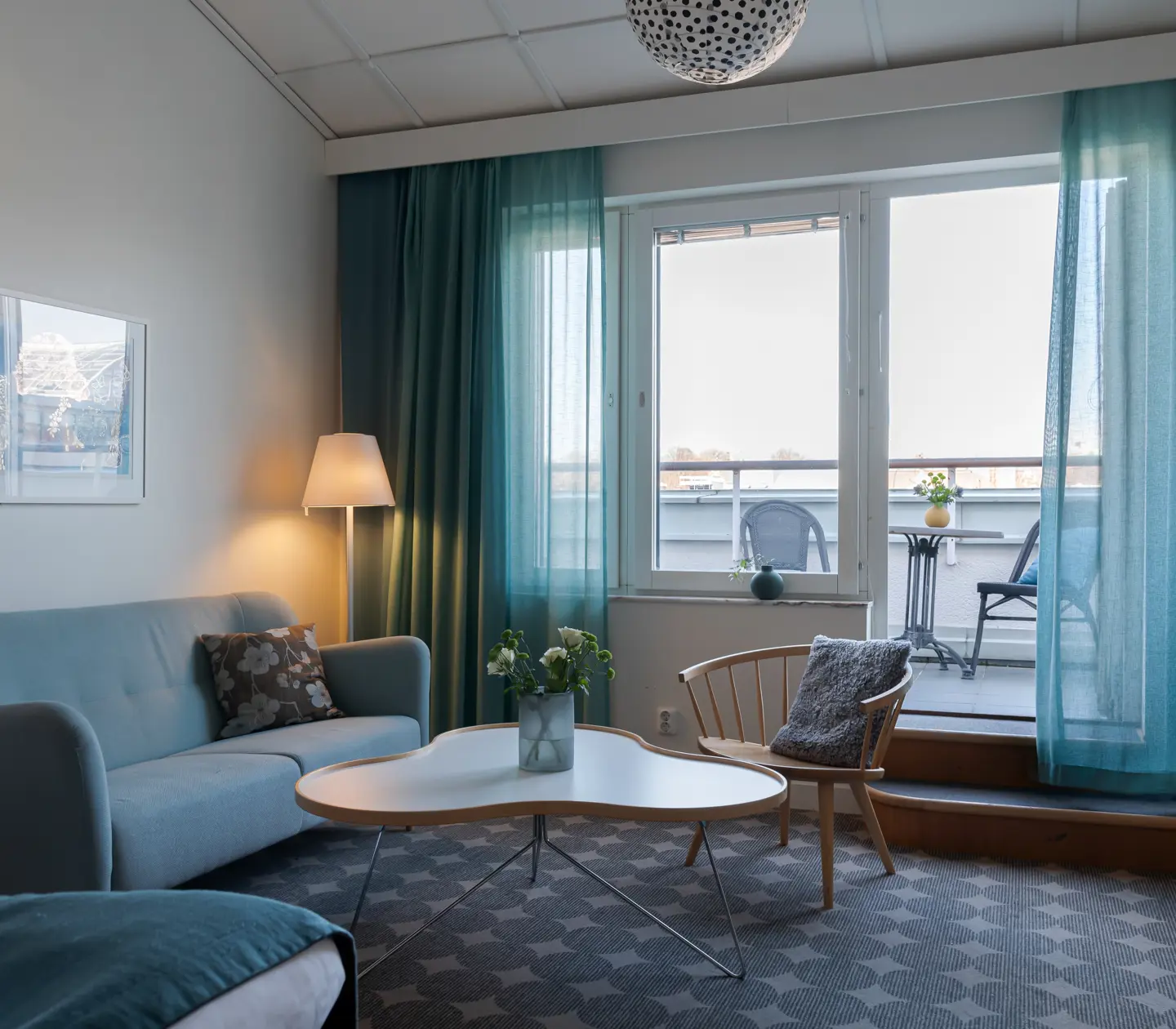 Bright hotel suite with sofa, balcony and blue curtains