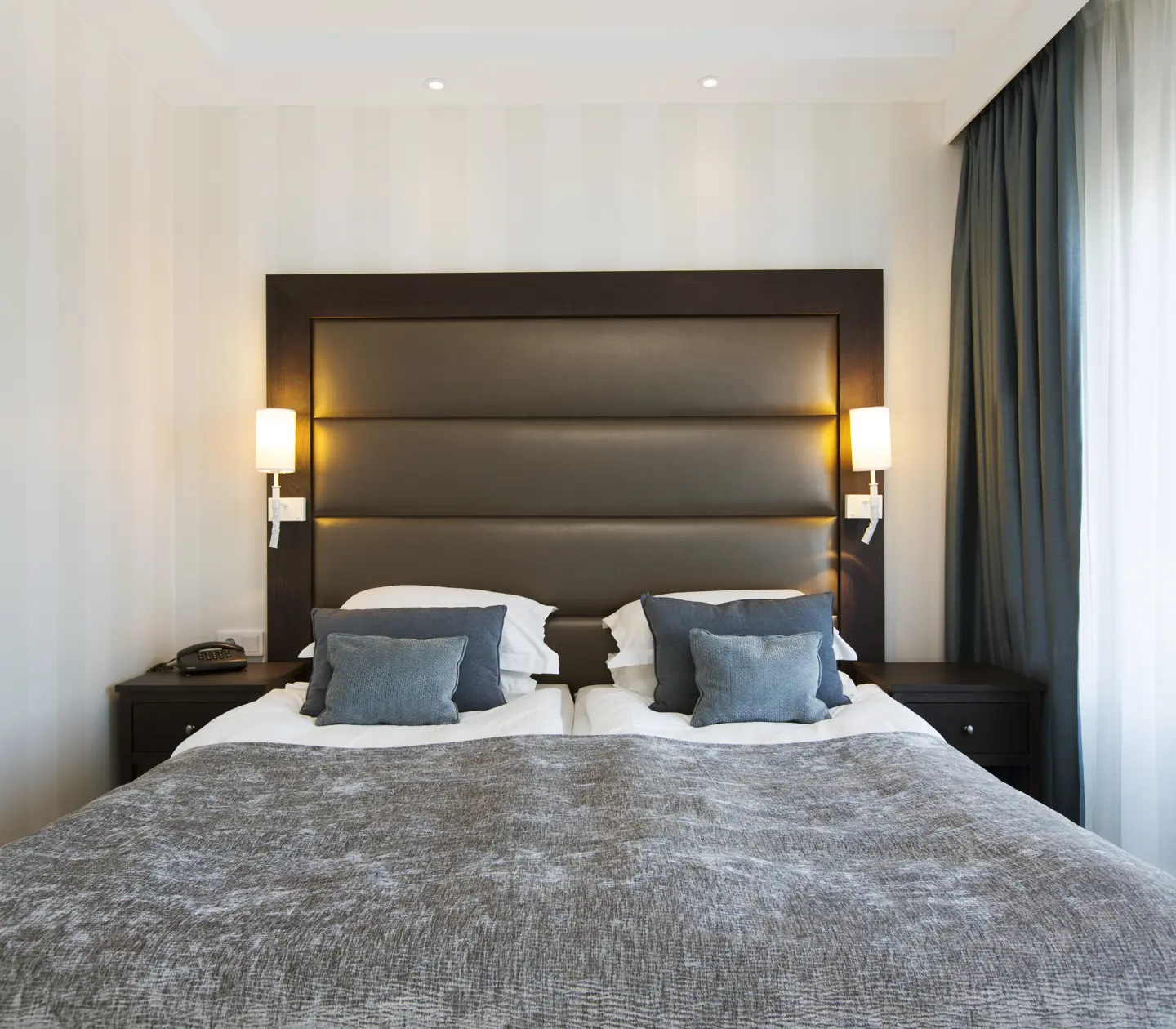 Bright hotel suite with bed, bedside lamps and blue pillows