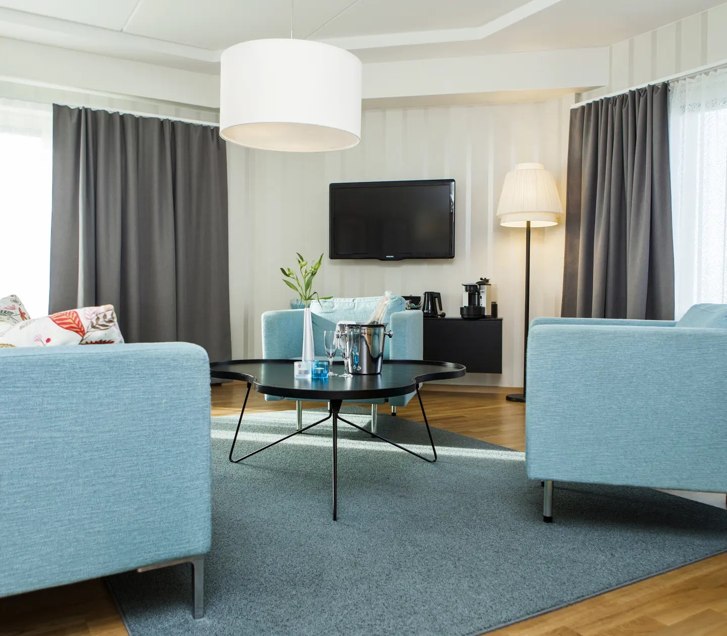 Bright hotel suite with blue sofa group, window and TV