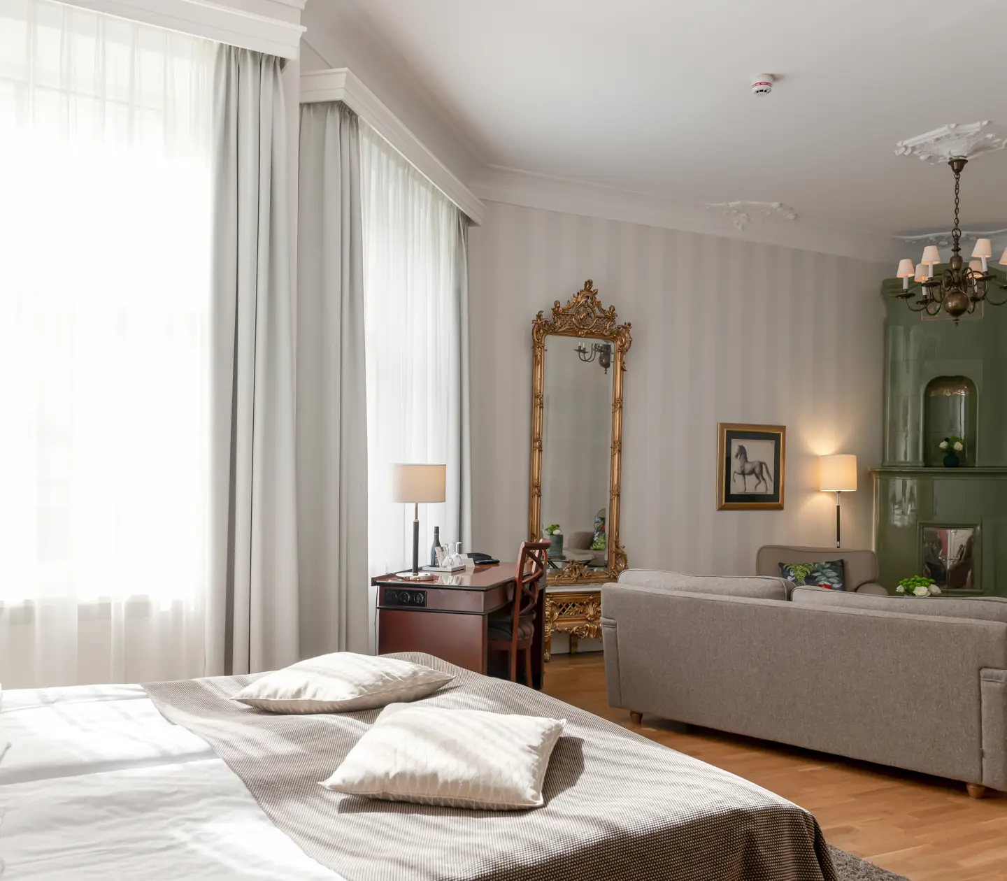 Bright hotel room with green tiled stove, bed and large windows