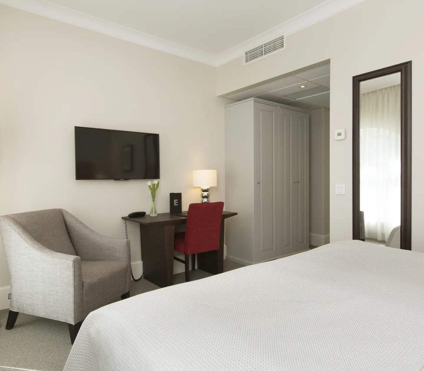 Bright hotel room with double bed, desk and armchair
