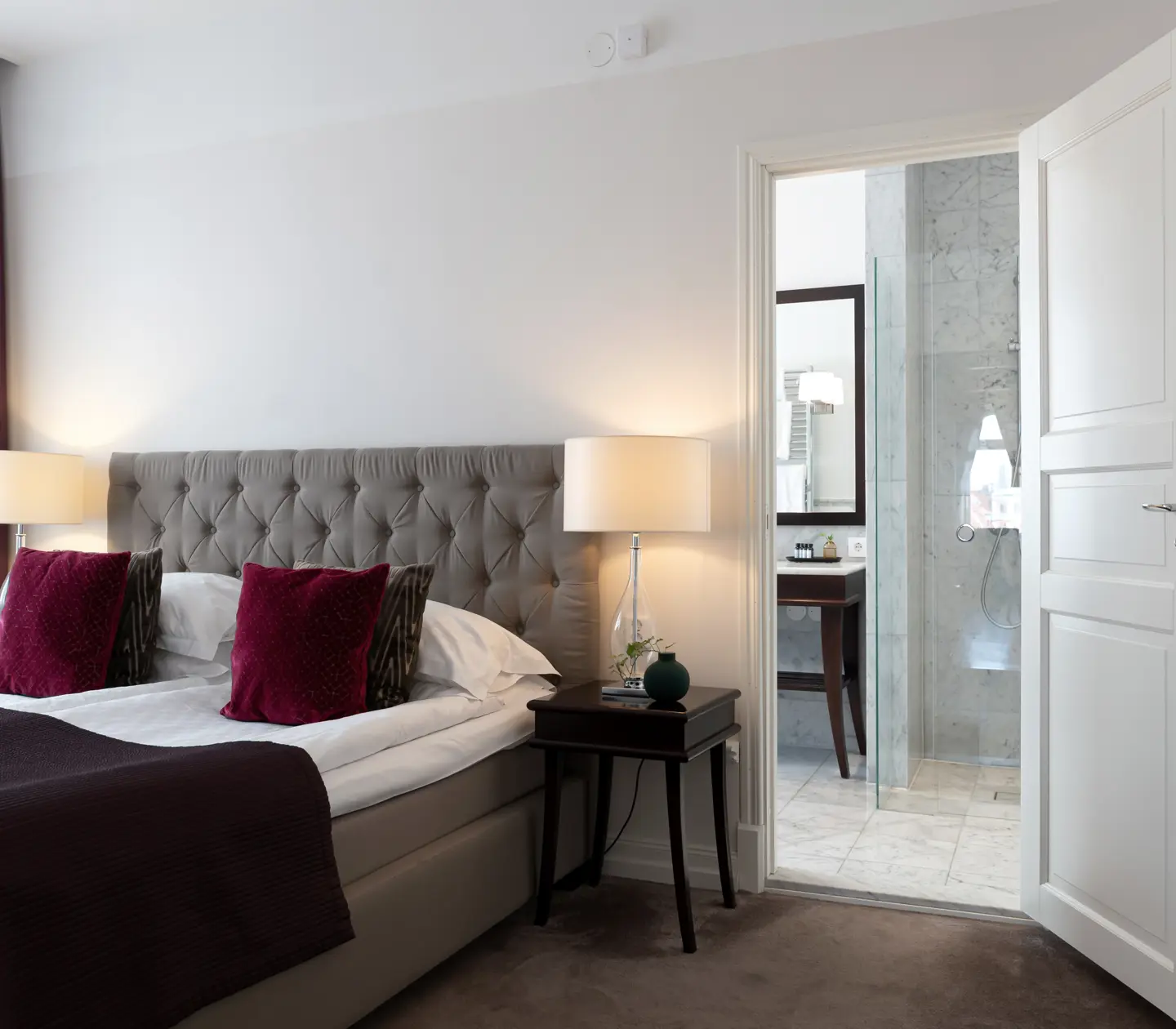 Suite with double bed, bedside lamps and door to bathroom